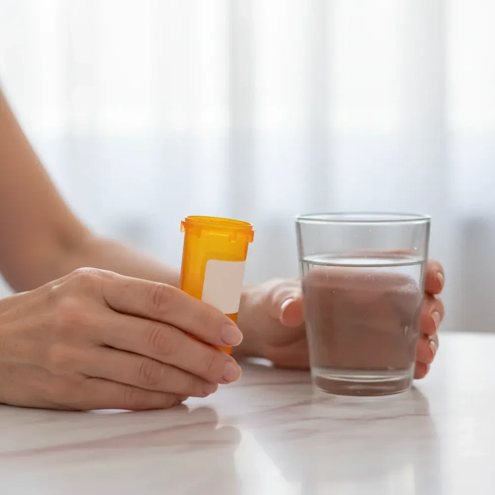 Close-up of hands holding a prescription pill bottle and a glass of water on a marble surface in soft side-light — Appetite Suppressant Medication at Jolie Visage in Murrells Inlet, SC