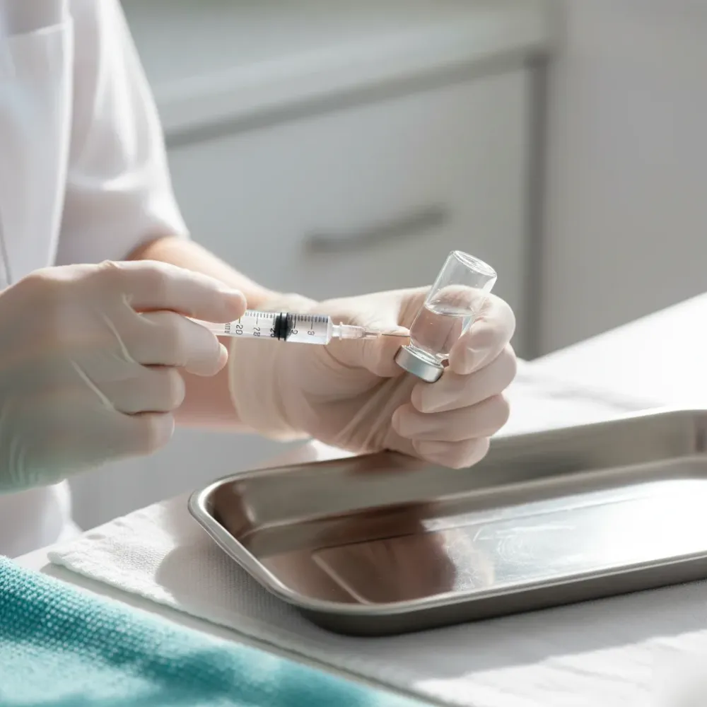 Provider's hands drawing a precise measurement from a glass vial over a clean stainless steel tray.